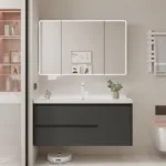 A sleek bathroom vanity with dark drawers and a large backlit mirror above. Minimalist design featuring a decorative plant and streamlined sink.
