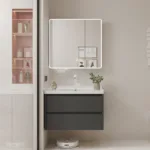Contemporary bathroom featuring a vanity with dark drawers, illuminated mirror, wall art, and shelves with toiletries.