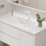 Sleek white bathroom vanity with integrated sink, chrome faucet, and a small plant in a vase on the countertop.